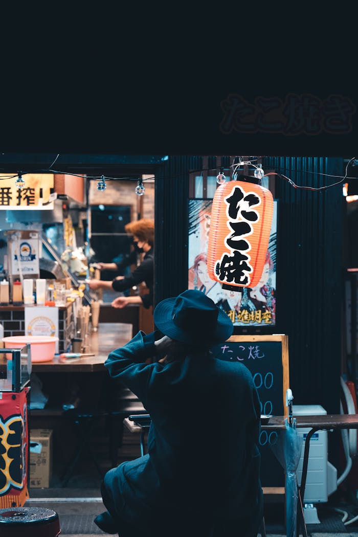 A person enjoys the ambiance of a Japanese street food vendor illuminated by vibrant signage.