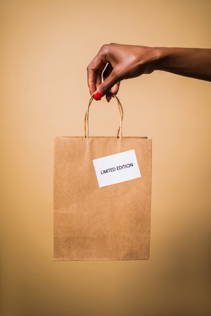 Close-up of a hand holding a brown paper shopping bag labeled 'Limited Edition' on an orange background.